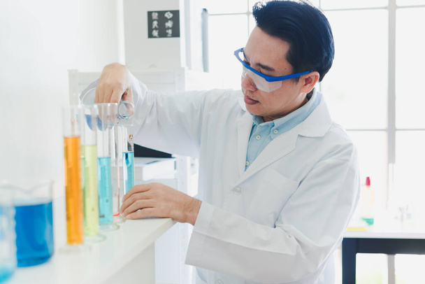 Asian scientists are preparing chemicals for testing and analysis in the laboratory. Scientists clear glasses and white shirts. Science and Chemistry Concept - Fotó, kép