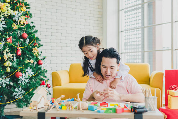 Asian father and daughter play toys on the table in the living room decorated with Christmas trees to prepare for Christmas and New Year's celebrations. - Valokuva, kuva