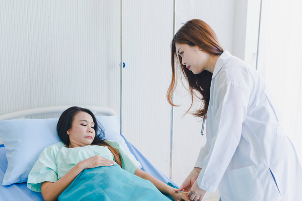 Ázsiai nő orvos meglátogatja a beteg fekszik a kórházi ágyban. - Fotó, kép