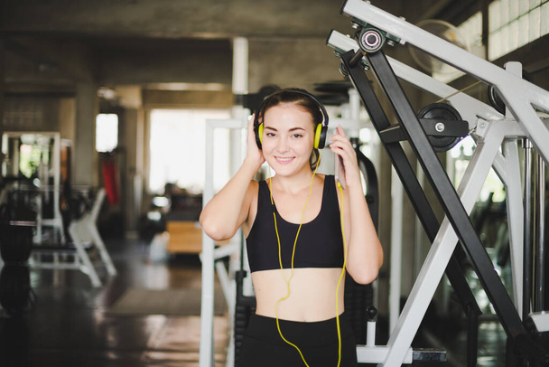 Beautiful women come to exercise in the gym and are relaxed by listening to music from headphones. She wears a sportswear. - Фото, изображение