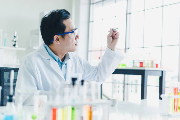 Asian scientists are preparing plant-based materials for testing and analysis in the laboratory. Scientists clear glasses and white shirts. Science and Chemistry Concept - Foto, afbeelding