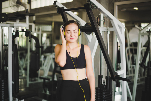Beautiful women come to exercise in the gym and are relaxed by listening to music from headphones. She wears a sportswear. - Zdjęcie, obraz
