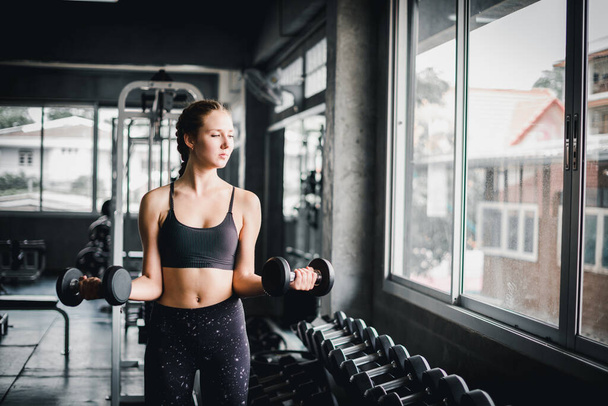 Beautiful female athletes are exercising in the gym. By lifting the dumbbell. The gym has a full range of exercise equipment. - Fotografie, Obrázek