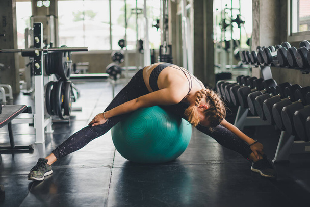 A beautiful woman wearing a sports shirt, stretching and relaxing with a rubber ball, yoga or exercise ball. - Foto, Bild