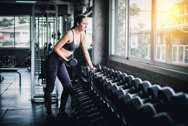 Beautiful female athletes are exercising in the gym. By lifting the dumbbell. The gym has a full range of exercise equipment. - Φωτογραφία, εικόνα