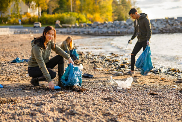 Giovane donna raccogliendo spazzatura in borsa in spiaggia
 - Foto, immagini