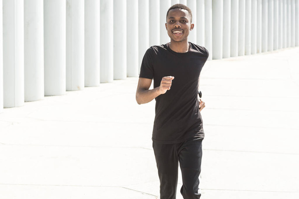 Athletic young afroamerican man running on the promenade. Black Male runner sprinting outdoors. Healthy lifestyle concept. - Φωτογραφία, εικόνα