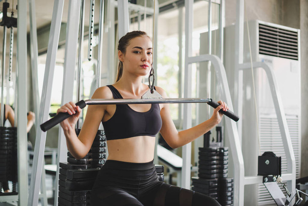 Beautiful athlete exercising with a lat pulldown machine to play the arms and shoulder muscles in the gym. Exercise in the gym concept. - Foto, Bild