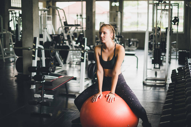 Красивая женщина в спортивной рубашке, растягиваясь и расслабляясь с резиновым мячом, йогой или тренировочным мячом
. - Фото, изображение