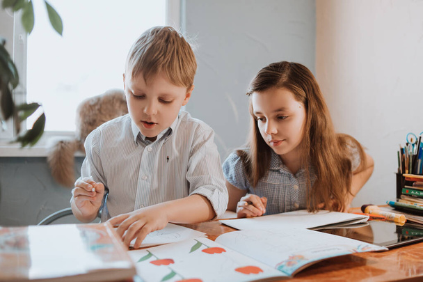 Der Junge und das Mädchen schreiben zu Hause während der CoVid-19-Quarantäne, Fernunterricht online mit dem Laptop, ein Kind macht Hausaufgaben für die Schule. Kinder blieben zu Hause. - Foto, Bild