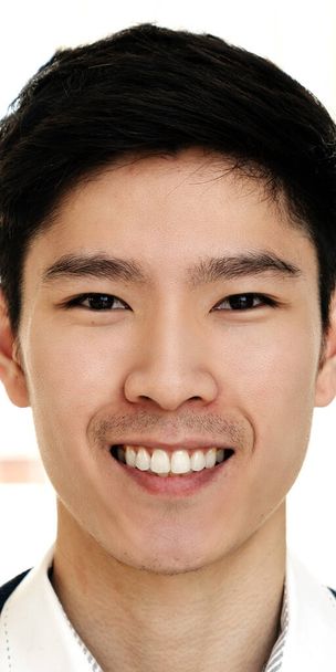 Portret van jonge aantrekkelijke Aziatische creatieve man glimlachend en kijkend naar camera in modern kantoor gevoel zelfverzekerd en positief. Hoofdfoto van Chinese mannelijke werknemer, ondernemer of student. - Foto, afbeelding