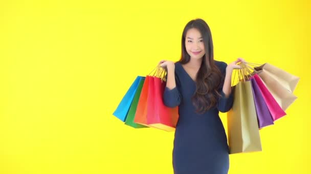 πλάνα από όμορφη ασιατική γυναίκα με πολύχρωμες τσάντες ψώνια απομονώνονται σε κίτρινο - Πλάνα, βίντεο