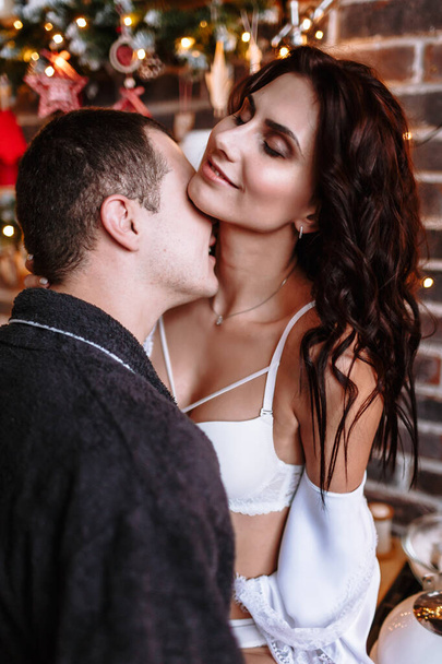 A guy and a girl in dressing gowns hug in the kitchen, decorated for Christmas - Photo, image
