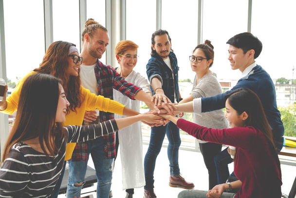 Multiethnic young team stack hands together as unity and teamwork in modern office. Diverse group togetherness collaboration or friends huddle concept. Startup business team building with soft tone. - Photo, Image