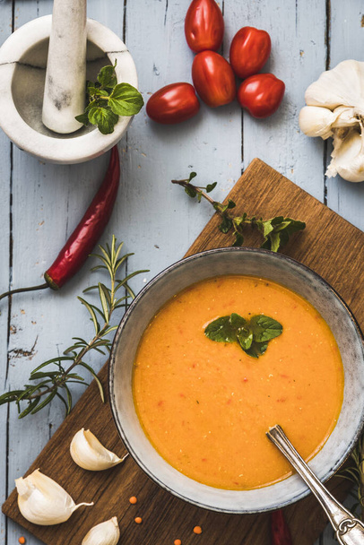 Deliciosa sopa de creme de lentilha colorida com ervas, tomates, pimentão e alho deitado em uma mesa cinza, vista superior, vertical
. - Foto, Imagem