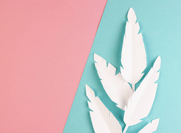 white paper feathers on a pink and blue background, top view. paper decoration on a pastel background - Foto, Imagem