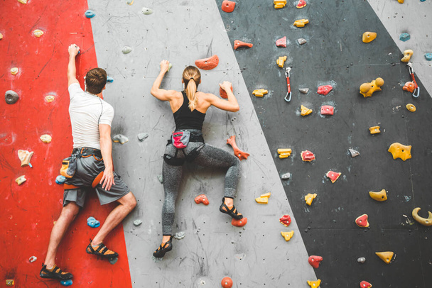 couple of athletes climber moving up on steep rock, climbing on artificial wall indoors. Extreme sports and bouldering concept - 写真・画像