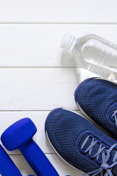 Sports set. Blue women's sneakers, blue dumbbells and white scales stand on a white wooden background - Photo, Image