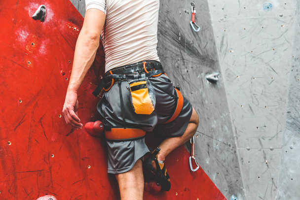 Sportsman climber moving up on steep rock, climbing on artificial wall indoors. Extreme sports and bouldering concept - Foto, Imagen