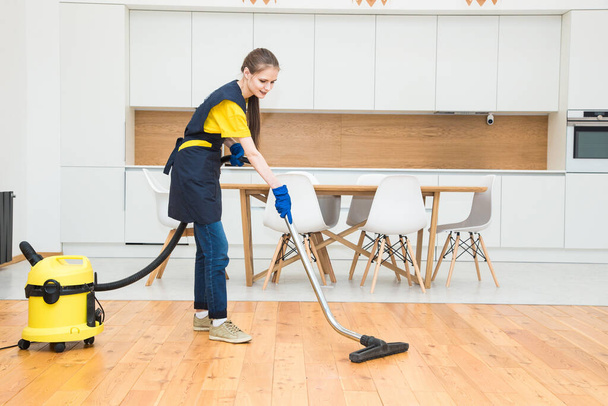 professional cleaning service. woman in uniform and gloves does the cleaning in a cottage. the worker vacuums the floor with professional equipment - Valokuva, kuva