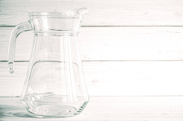 Порожній скляний карафе для води стоїть на білому дерев'яному тлі. Крупним планом
 - Фото, зображення