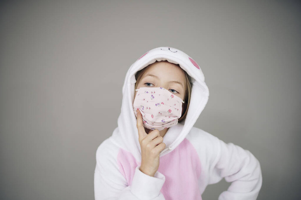beautiful girl in easter bunny costume and face protective mask posing on grey background, concept of easter during coronavirus lockdown  - Фото, изображение
