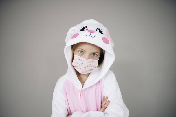 beautiful girl in easter bunny costume and face protective mask posing on grey background, concept of easter during coronavirus lockdown  - Φωτογραφία, εικόνα
