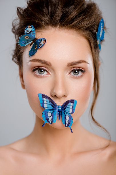 красивая молодая женщина с декоративными бабочками на лице изолированы на сером
  - Фото, изображение