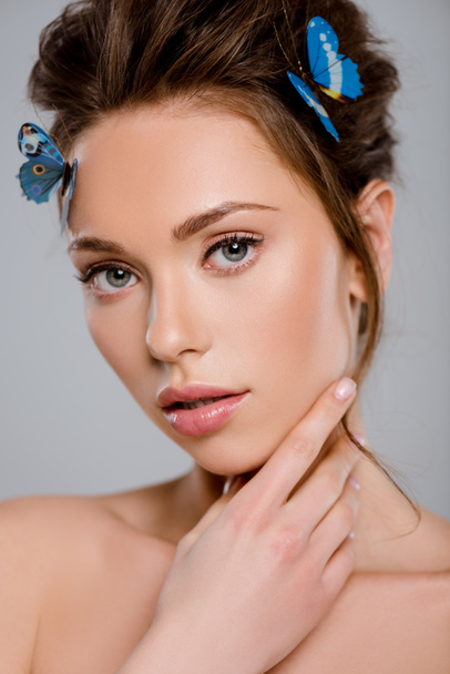 beautiful girl with decorative butterflies on hair touching face isolated on grey  - Фото, изображение
