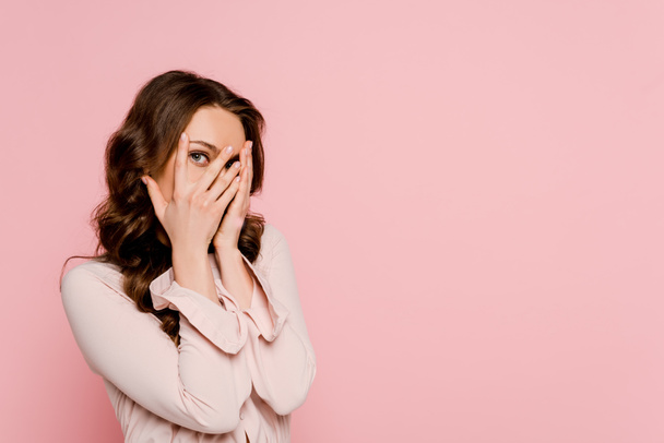 scared woman covering face and looking at camera isolated on pink  - Foto, Imagen