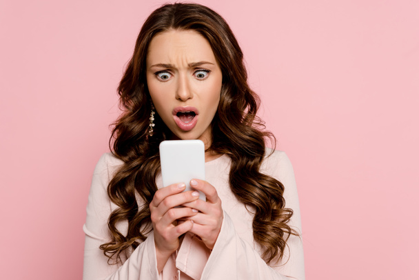 shocked girl looking at smartphone isolated on pink  - Foto, Imagem