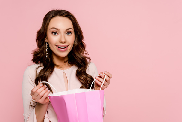 happy young woman holding shopping bag isolated on pink  - Valokuva, kuva