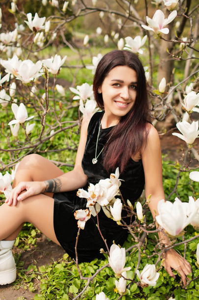 Beautiful girl in a black dress with blooming magnolias. - Fotoğraf, Görsel