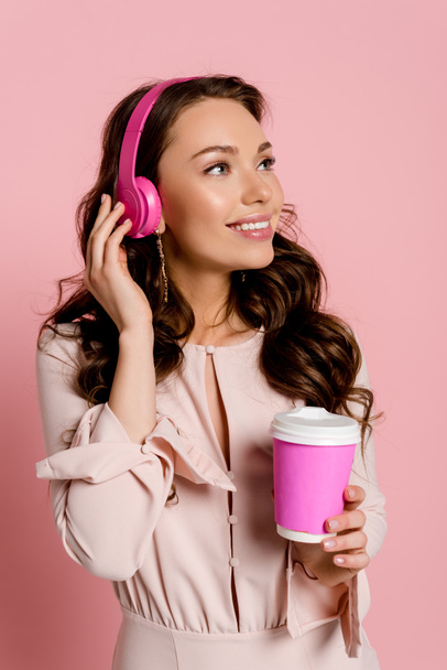 happy girl listening music in wireless headphones and holding paper cup on pink  - Foto, Imagem