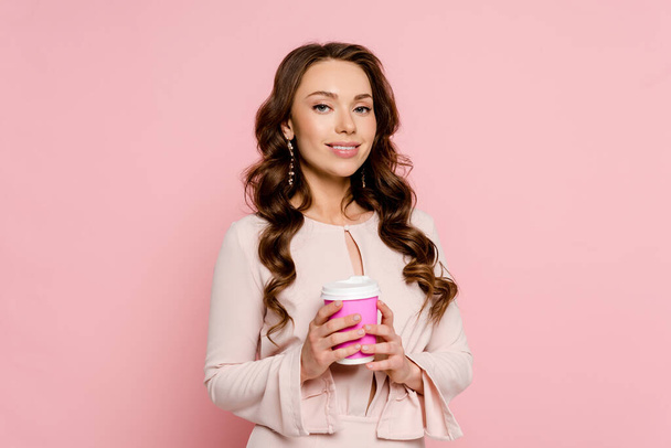 happy young woman holding paper cup isolated on pink  - Foto, imagen