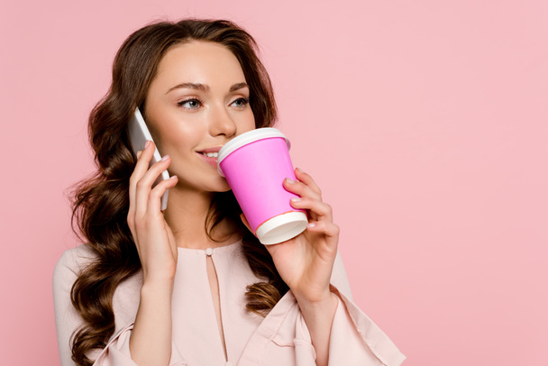 χαρούμενο κορίτσι που μιλάει στο smartphone και πίνει καφέ για να απομονωθεί στο ροζ  - Φωτογραφία, εικόνα