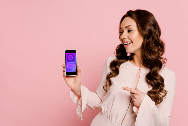 ragazza allegra che punta con il dito allo smartphone con lo shopping online sullo schermo isolato su rosa
  - Foto, immagini