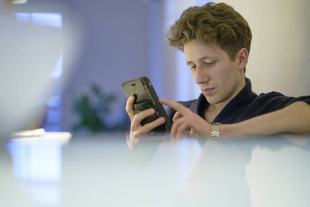 Portret młodego przystojniaka patrzącego na telefon komórkowy w jego rękach to mieszkanie. - Zdjęcie, obraz