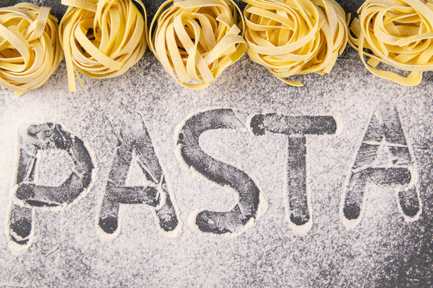 Homemade uncooked pasta tagliatelle on black background. Making fresh italian tagliatelle . The word 'pasta' from flour. Banner. - Fotoğraf, Görsel