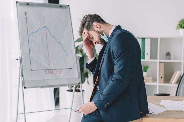side view of stressed businessman standing with bowed head and closed eyes near flipchart with graphs showing recession - Photo, Image