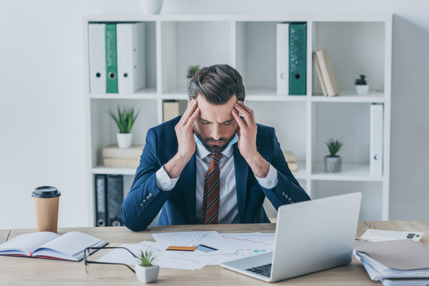 depressed businessman touching bowed head while sitting with closed eyes at workplace - Photo, Image
