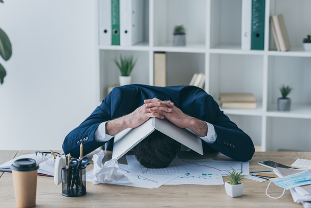 depressziós üzletember ül a munkahelyen és laptoppal fedi le a fejét - Fotó, kép