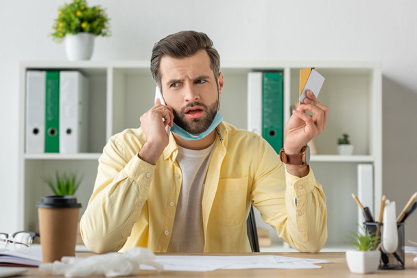 enfoque selectivo del hombre de negocios preocupado hablando en el teléfono inteligente mientras sostiene tarjetas de crédito
 - Foto, Imagen