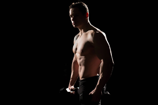 Musculoso y en forma joven culturista fitness modelo masculino posando sobre fondo negro. - Foto, imagen