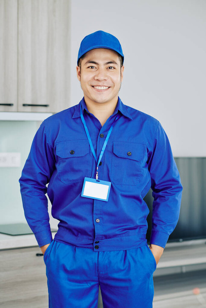 Mavi üniformalı ve şapkalı, kameraya gülümseyen, kendinden emin Vietnamlı işçinin portresi. - Fotoğraf, Görsel