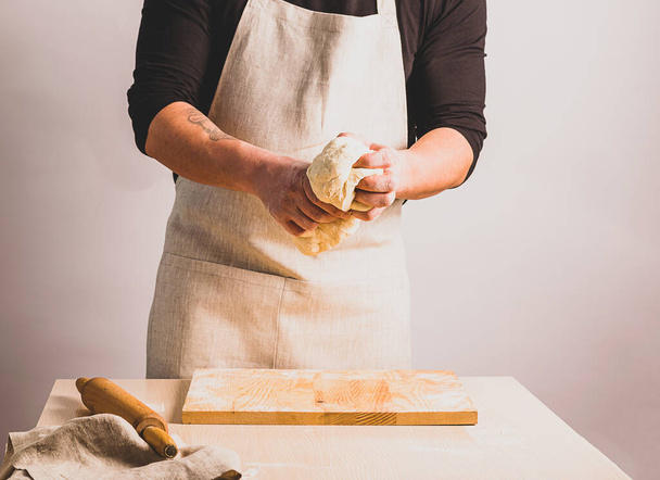Un hombre en un delantal amasa la masa hace pan. El concepto de hornear hecho en casa. Enfoque selectivo
. - Foto, imagen