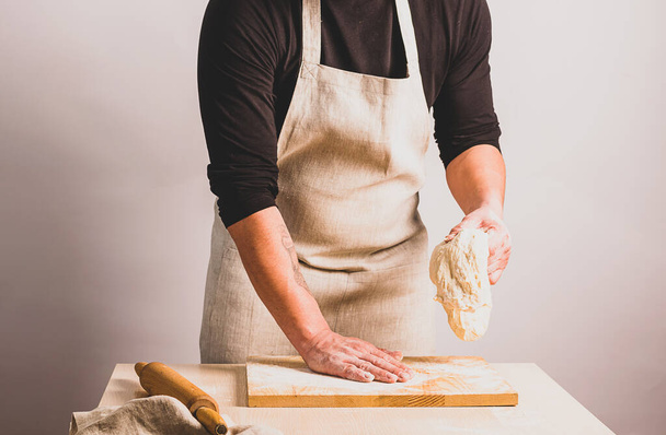 Un homme dans un tablier pétrit la pâte pour faire du pain. Le concept de la cuisson maison. Concentration sélective
. - Photo, image