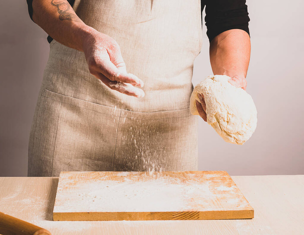 A man in an apron kneads the dough makes bread. The concept of home-made baking. Selective focus. - Zdjęcie, obraz