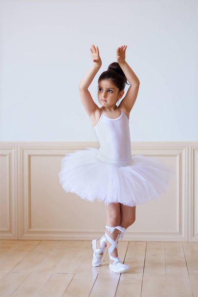 Little girl ballerina in a white tutu is on the floor in ballet class. - Zdjęcie, obraz