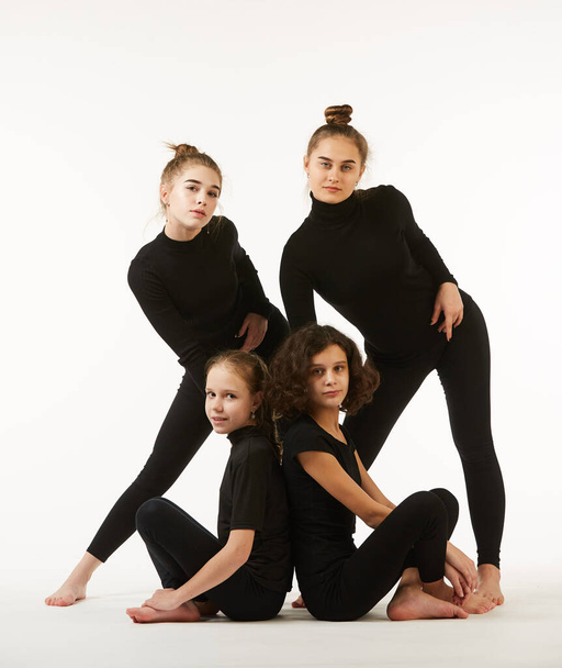 Cztery dziewczyny w różnym wieku w pozach tanecznych i czarne ubrania są kręcone na białym tle. - Zdjęcie, obraz